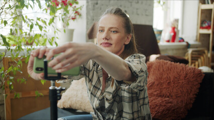 A woman takes a smartphone from a tripod and watches the recorded video. She is happy with the result