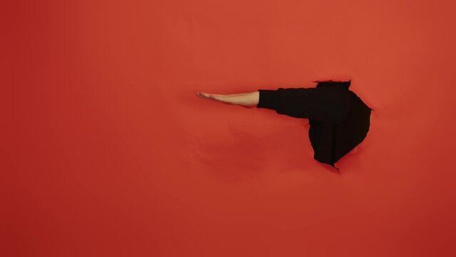 Man's hand playing game of rock paper scissors from hole of orange background in studio. Unrecognizable person playing manual game.