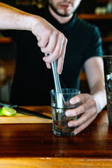 detail of the hands of a young and modern waiter, crushing the mojito ingredients to release their juices . vertical