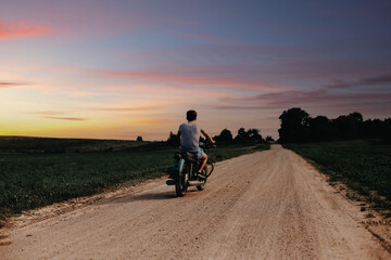 young man rides on a country road on a retro vintage motorcycle, a biker rides at sunset.