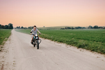 Obraz premium young joyful man rides a retro motorcycle on a country road. The concept of a biker in his youth in the countryside.