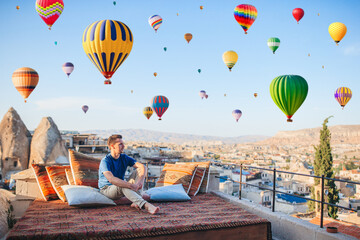 Happy young man watching hot air balloons in Cappadocia, Turkey - obrazy, fototapety, plakaty