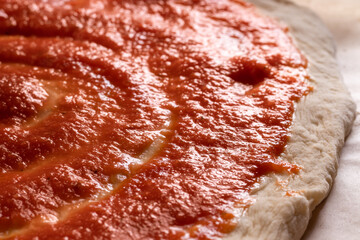 Raw pizza, preparation in traditional style. Adding tomato sauce on a pizza dough.