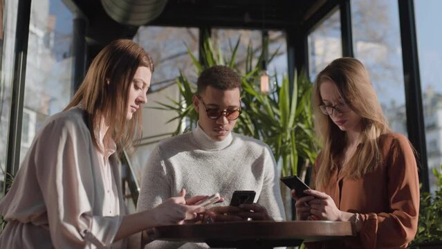 Three friends in a cafe bar using phone. Looking at smartphones unconscious about the surroundings..
