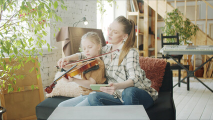 The older sister is engaged in music with the child. The girl plays the violin and the woman keeps © iaginzburg