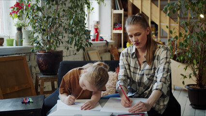 A girl and her mother draw together with colored pencils sitting on the couch