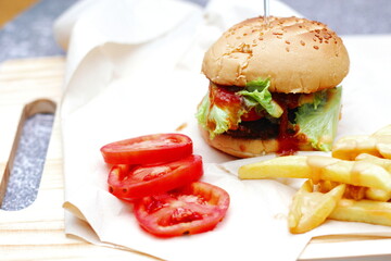 Home made hamburgers served with french fries and tomatoes on a wooden table. Fast food and junk food.
