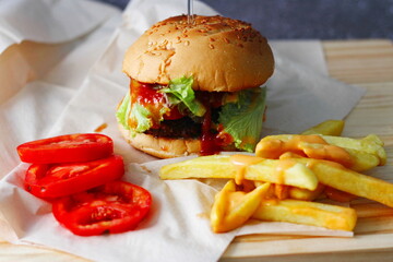 Home made hamburgers served with french fries and tomatoes on a wooden table. Fast food and junk food.