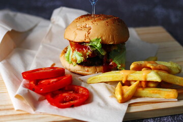 Home made hamburgers served with french fries and tomatoes on a wooden table. Fast food and junk food.