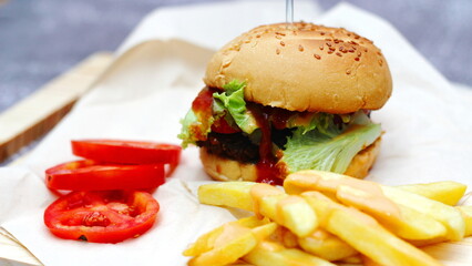 Home made hamburgers served with french fries and tomatoes on a wooden table. Fast food and junk food.