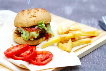 Home made hamburgers served with french fries and tomatoes on a wooden table. Fast food and junk food.