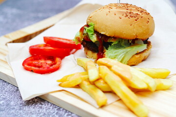 Home made hamburgers served with french fries and tomatoes on a wooden table. Fast food and junk food.