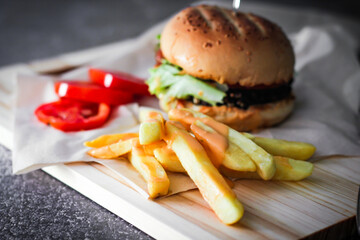 Home made hamburgers served with french fries and tomatoes on a wooden table. Fast food and junk food.