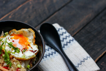 Japanese-style fried rice served in a black bowl with a fried egg and red tomato slices.