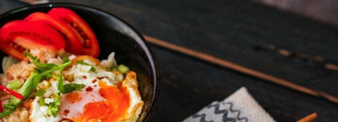 Japanese-style fried rice served in a black bowl with a fried egg and red tomato slices.