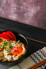 Japanese-style fried rice served in a black bowl with a fried egg and red tomato slices.
