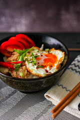 Japanese-style fried rice served in a black bowl with a fried egg and red tomato slices.