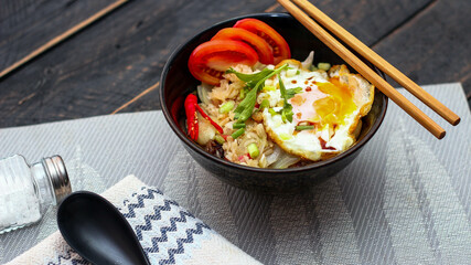 Japanese-style fried rice served in a black bowl with a fried egg and red tomato slices.
