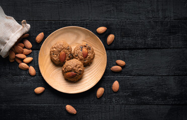 Almond cookies in wooden bowl on old black wooden background Almonds and seeds in freely arranged sacks Delicious organic pastries.
