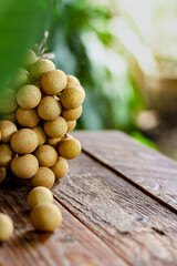 bunch of longan is placed on a wooden table with green leaves behind.