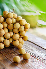 bunch of longan is placed on a wooden table with green leaves behind.