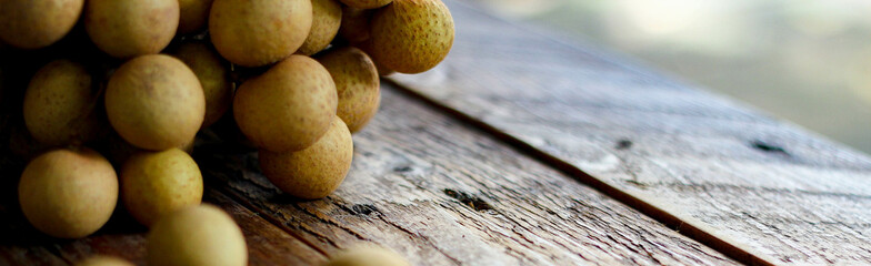 bunch of longan is placed on a wooden table with green leaves behind.