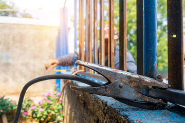 Earth clamp nailed to a metal fence while a blue collar worker making repairs outdoors