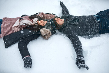 The snow make us feel like kids again. High angle shot of a couple lying in the snow making snow...