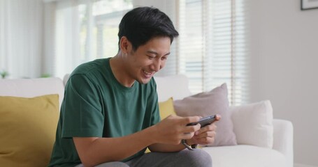 Asia people young man relax sitting easy at home sofa couch laugh smile enjoy play video game social media on mobile app, win online stream casino battle trade, leisure teen activity happy fun joy.
