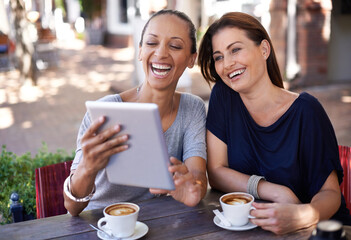 Laughing along with social media. Two young women looking at a tablet in a coffee shop.