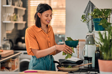 Leafy greens add goodness to any meal. Shot of a happy young woman preparing a healthy meal at home.