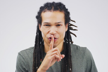 Dont tell anyone okay. Portrait of a handsome young man posing with his finger on his lips against a grey background.