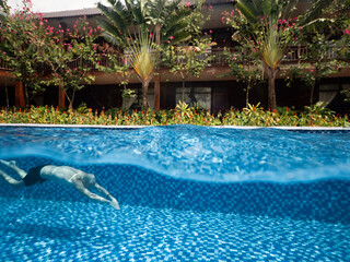 Tropical Villa with flowers and trees and pristine swimming pool with a man swimming.