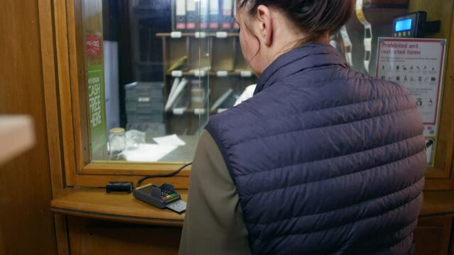 Woman paying for parcel at post office with credit bank card.