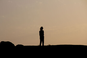 Silhouette of seductive woman on rooftop at urban sunset, Back view silhouette of unrecognizable female is watching sunset alone in sunny autumn evening in countryside