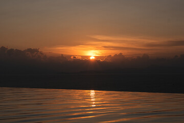 Landscape image of a sunset sky over infinity swimming pool and the sea