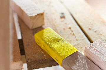 Sandpaper of yellow color is nailed to a wooden beam with steel staples close-up