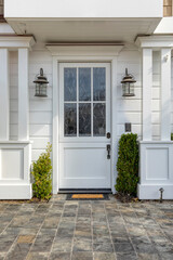 Front door that is white in color with two lamp fixtures, potted plants and a cool tile pattern showing off the entrance.