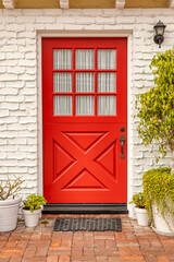 Country inspired front door that is red with a white brick wall.