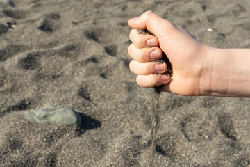 a hand pours dark sand on the beach