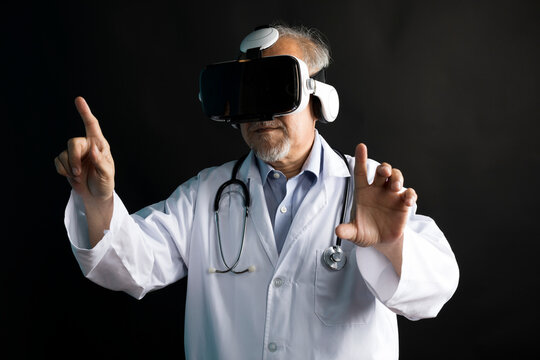 Telemedicine concept, old Asian doctor in lab uniform wearing VR glasses and operating medical task standing on black background.