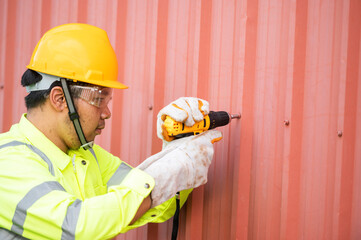 Caucasian construction worker working with a cordless electric screwdriver on a steel fence,cordless drill