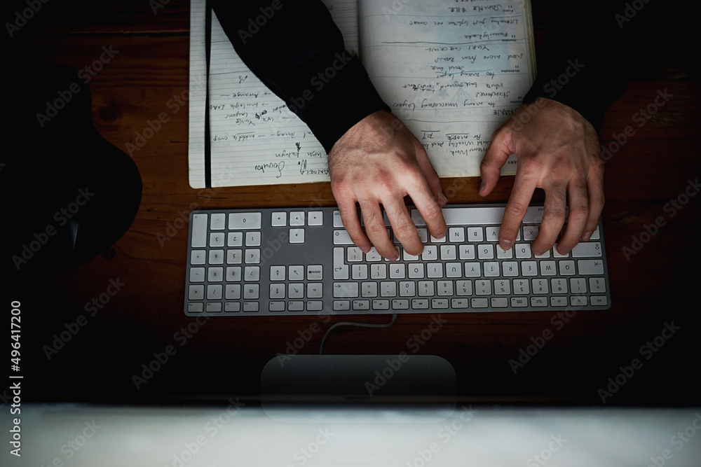 Poster doing what he does best. high angle shot of an unidentifiable hacker using a computer late at night.