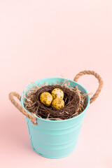 Small turquoise bucket with nest of colored golden quail eggs on pastel pink. Mock up.