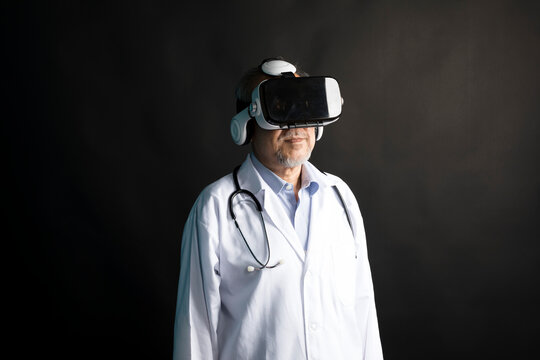 Telemedicine concept, old Asian doctor in lab uniform wearing VR glasses on black background.