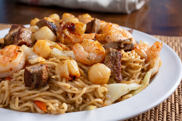 A view of a plate of chow mein, featuring toppings of beef, shrimp, and scallop. 