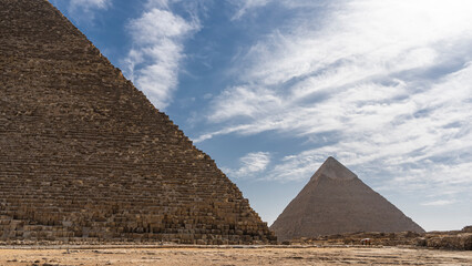 Obraz na płótnie Canvas Two great pyramids: Cheops and Chephren on a background of blue sky and clouds. The ancient masonry walls are visible. Egypt. Giza