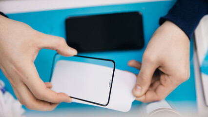 Repairman worker sticks protective glass on repaired phone, top view