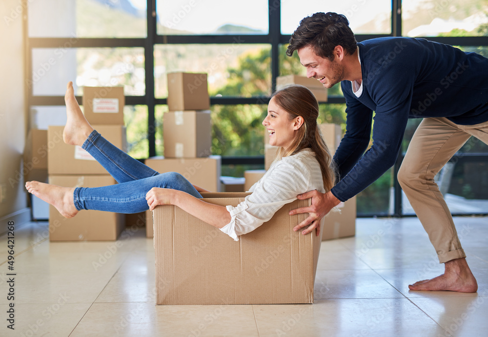 Sticker Filling their new home with fun. Shot of a young man pushing his girlfriend around in a box while they move into their new home together.