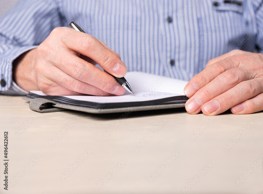 Poster Man taking notes in planner. Hands closeup writing information, agenda, reminders with pen in notebook. Businessman sitting at desk and working or studying. High quality photo
